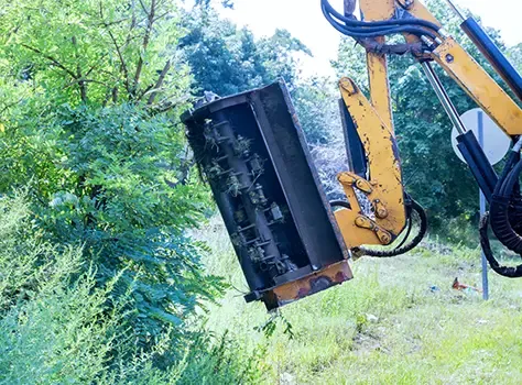 Flail attachment clearing vegetation beside a site boundary.